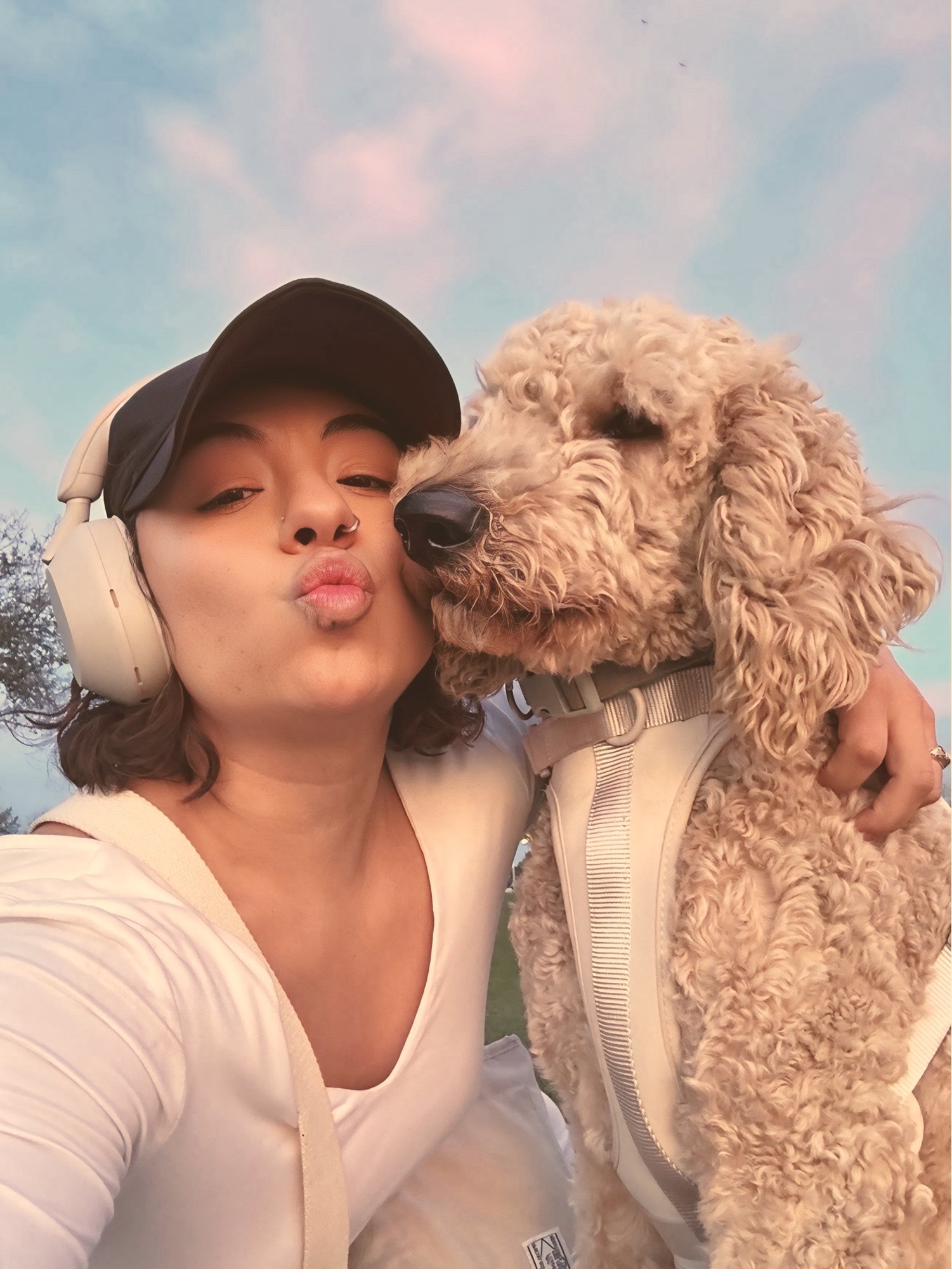 Eveling with her fluffy cream-colored dog against a pink sky