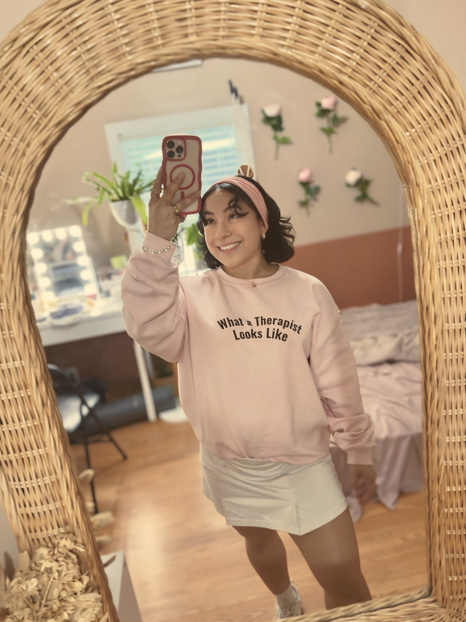 Eveling taking a mirror selfie in a pink sweatshirt that reads What a Therapist Looks Like